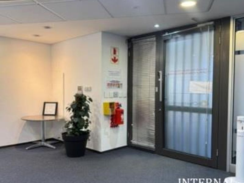 A professional office space featuring carpeted flooring, a suspended ceiling with recessed lighting, and a secure glass entrance door.