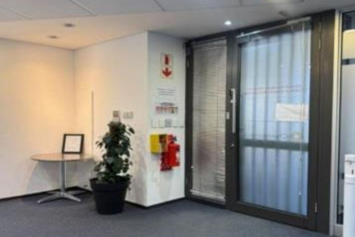 A professional office space featuring carpeted flooring, a suspended ceiling with recessed lighting, and a secure glass entrance door.