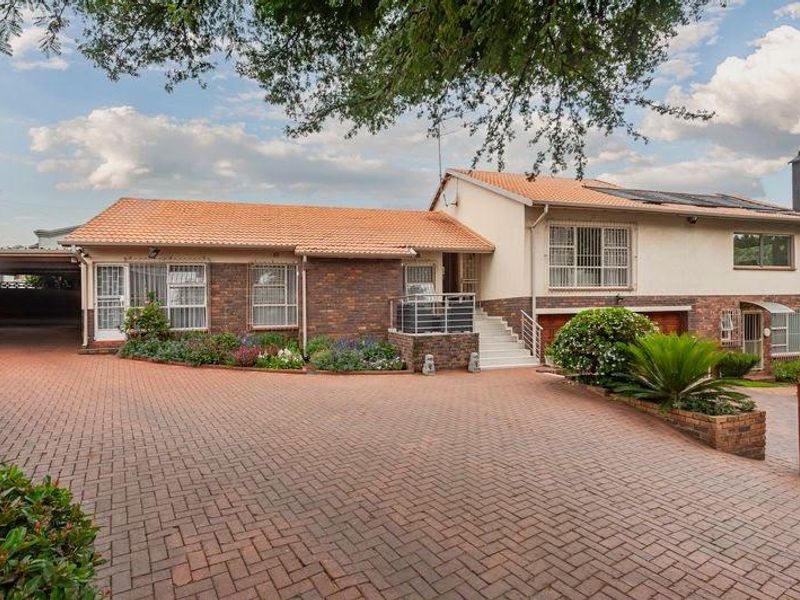 Front view of a multi-level brick house featuring a spacious paved driveway, tiled roof, integrated carport, and established garden beds.