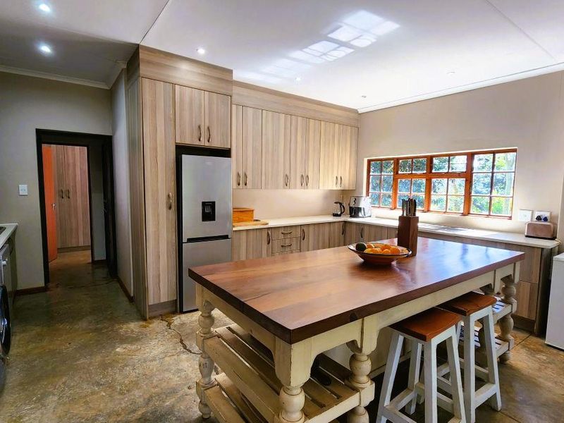Spacious kitchen featuring wood-look cabinetry, a large central island with a wooden countertop, and polished concrete flooring with natural light from a large window.