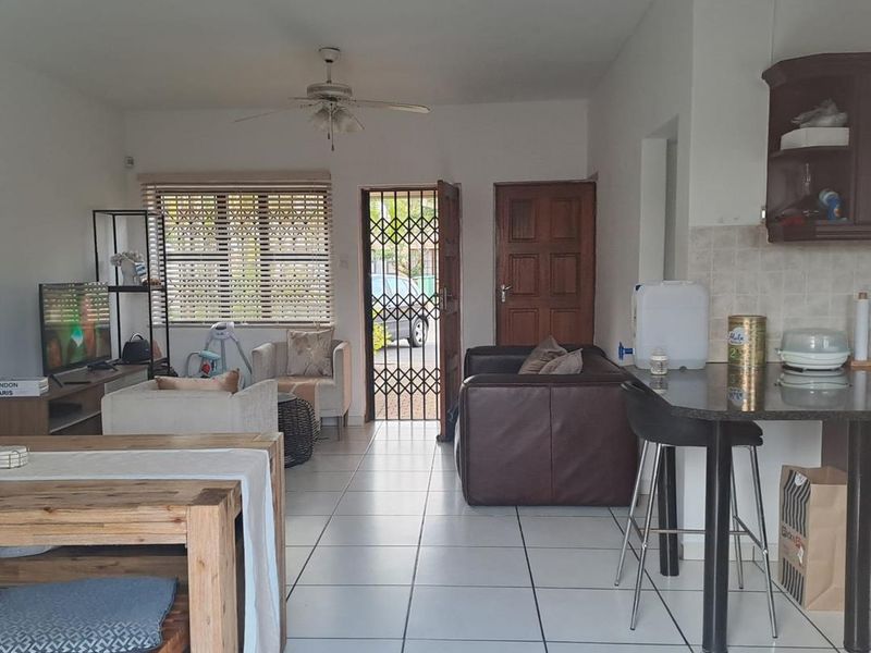 Open-plan living and kitchen area featuring tiled flooring, a breakfast bar, and direct access to the exterior through a security gate.