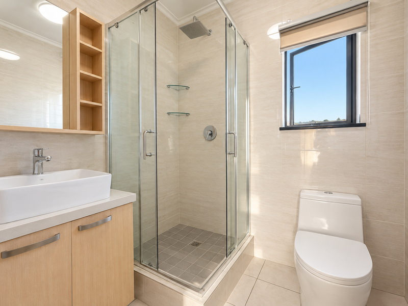 A modern, well-maintained bathroom featuring a vessel sink vanity, a glass-enclosed shower with a rain shower head, and a clean, neutral tiled finish.