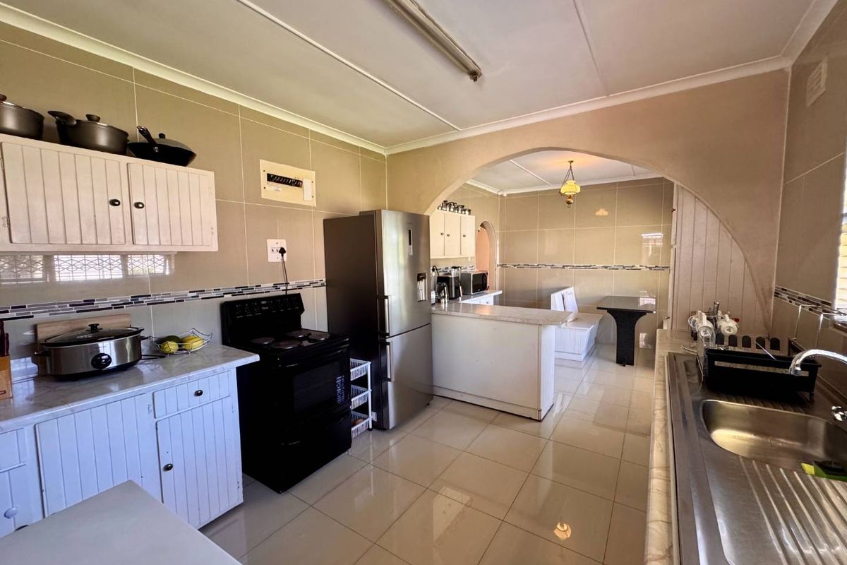 A functional kitchen featuring tiled walls and floors, built-in cabinetry, a stainless steel sink, and an arched opening leading to an adjacent dining area.