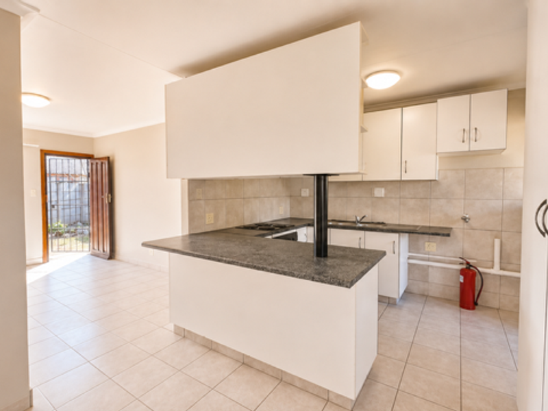 Open-plan kitchen and living area featuring tiled flooring, built-in cabinetry, and direct access to the exterior through a security gate.
