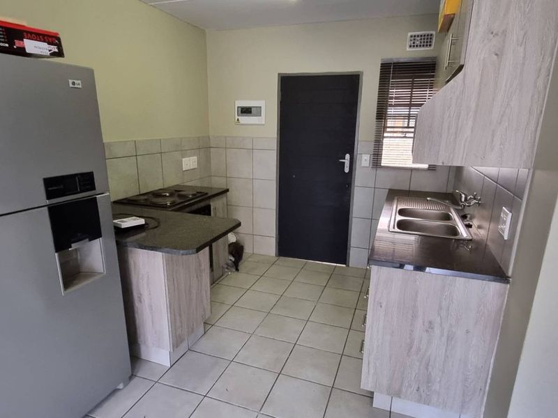 Functional kitchen featuring light wood-look cabinetry, dark laminate countertops, tiled backsplash, and ceramic floor tiles with a built-in hob and sink.