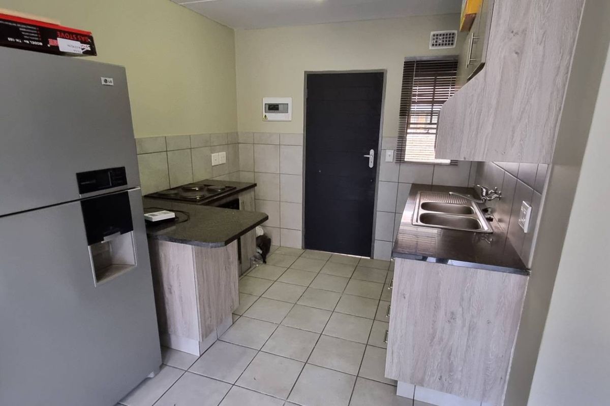 Functional kitchen featuring light wood-look cabinetry, dark laminate countertops, tiled backsplash, and ceramic floor tiles with a built-in hob and sink.
