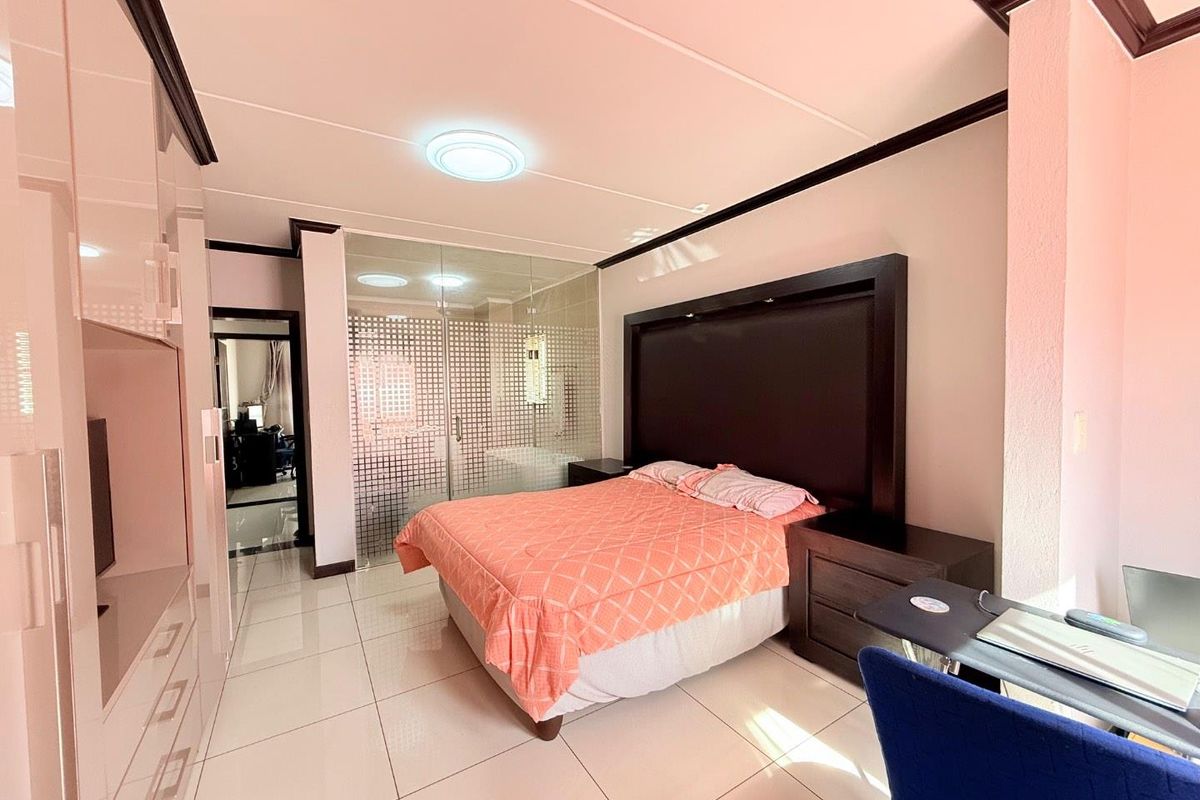 A bedroom featuring tiled flooring, built-in cabinetry, and an integrated glass-enclosed en-suite bathroom.