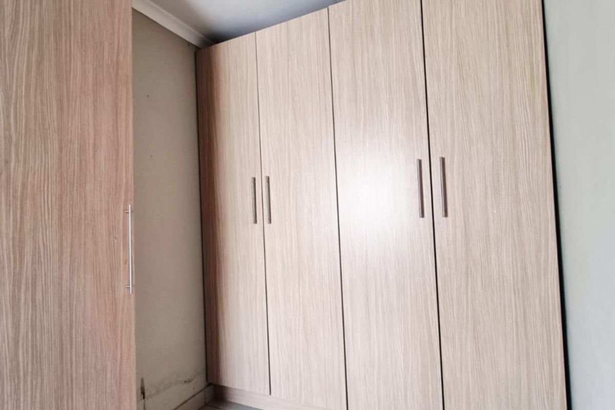 A bedroom featuring light wood-finish built-in cupboards and tiled flooring, showing signs of wall dampness and ceiling wear.