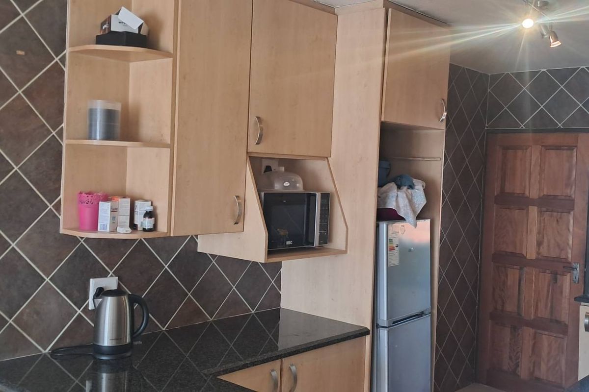 A functional kitchen featuring light wood cabinetry, dark granite countertops, and diamond-patterned wall tiling.