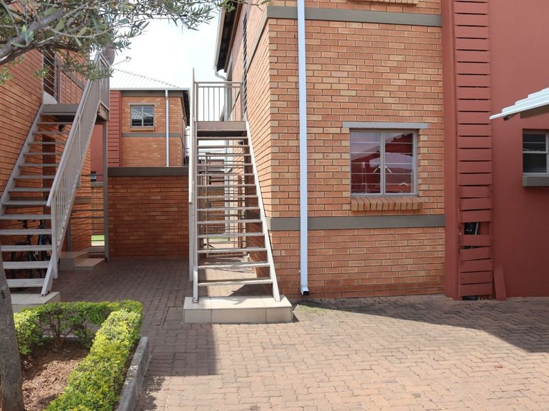 Exterior view of an apartment complex featuring brick facade, paved courtyard area, and external metal staircases providing access to upper levels.