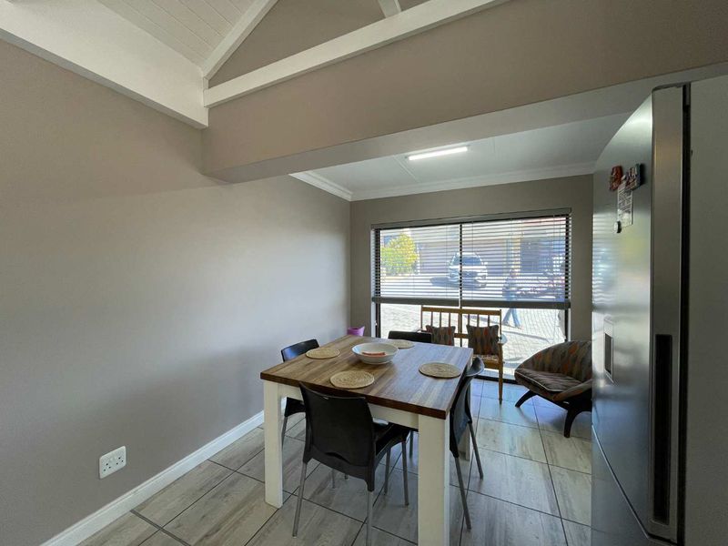 A dining area featuring vaulted ceilings with exposed rafters, tiled flooring, and large windows with venetian blinds allowing natural light.