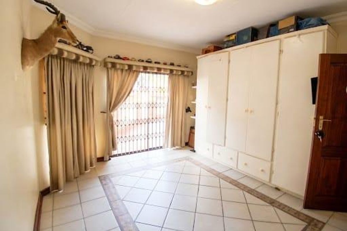 A bedroom featuring tiled flooring, built-in cupboards for storage, and a security gate over the window.