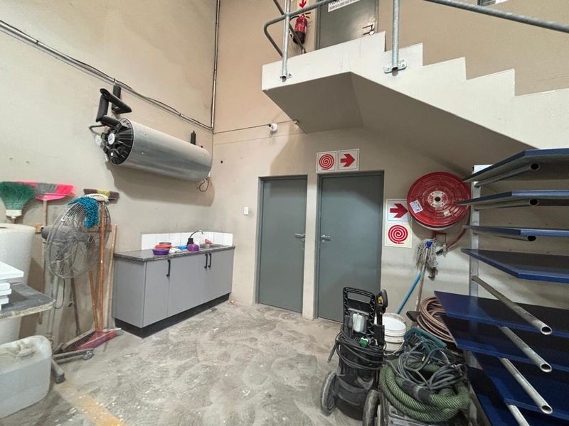 Industrial utility space featuring built-in cabinetry with sink, fire safety equipment, and access to an overhead mezzanine level via a metal staircase.