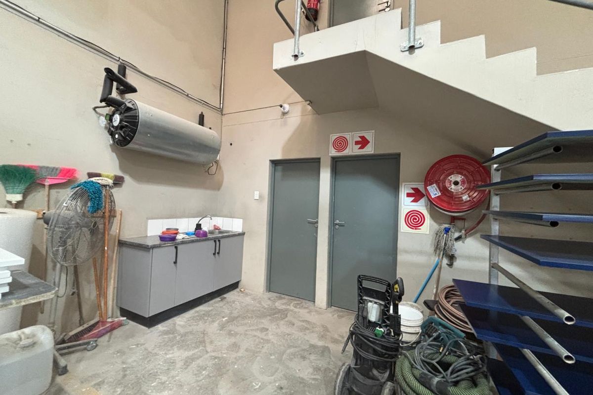 Industrial utility space featuring built-in cabinetry with sink, fire safety equipment, and access to an overhead mezzanine level via a metal staircase.