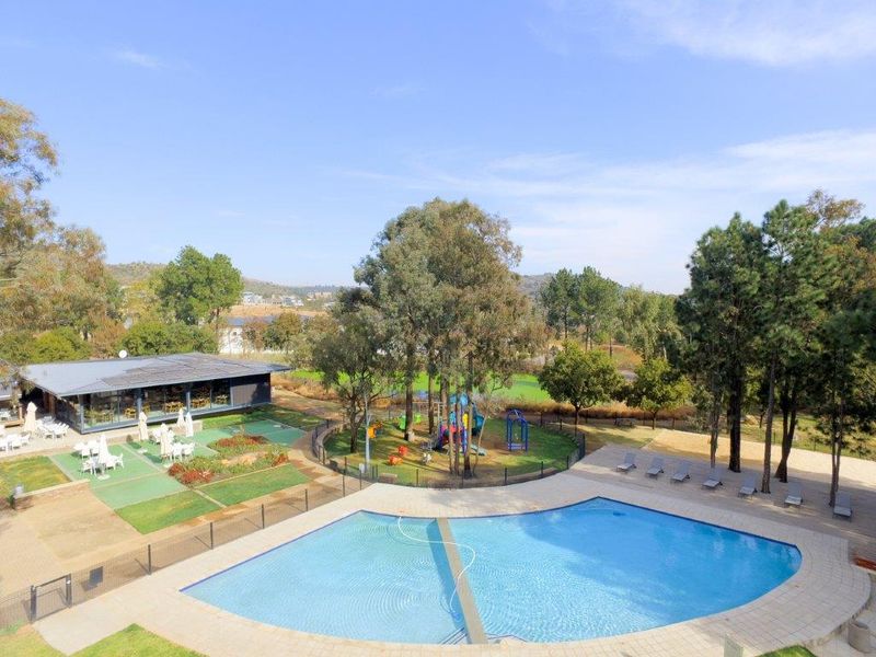 Aerial view of a residential estate featuring a swimming pool, playground, landscaped gardens, and a clubhouse facility.