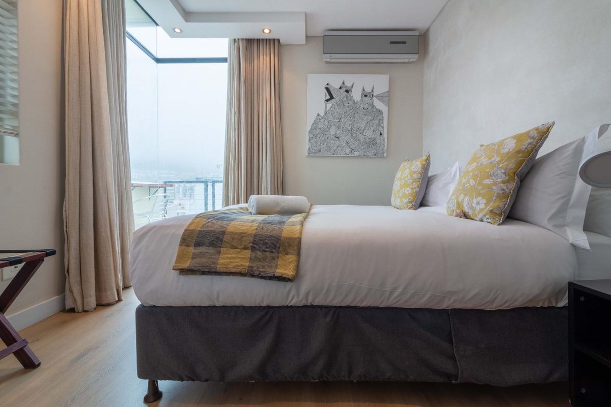 Modern bedroom featuring laminate flooring, recessed ceiling lighting, a wall-mounted air conditioning unit, and large floor-to-ceiling windows with natural light.