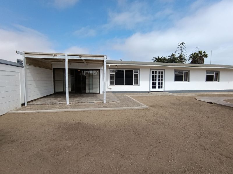 Rear view of the house featuring a covered patio area, paved walkways, and access through sliding and french doors.