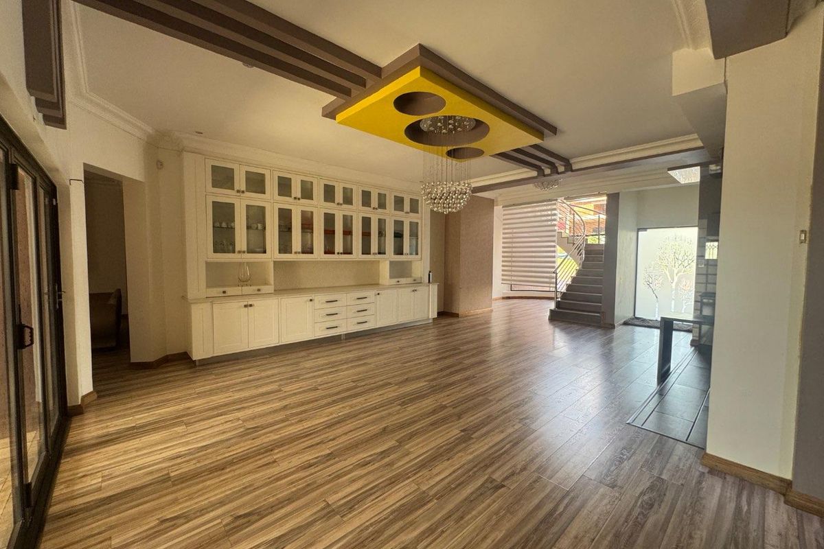 Spacious living area featuring wood-look flooring, extensive built-in cabinetry, and a unique recessed ceiling design with a staircase leading to the upper level.