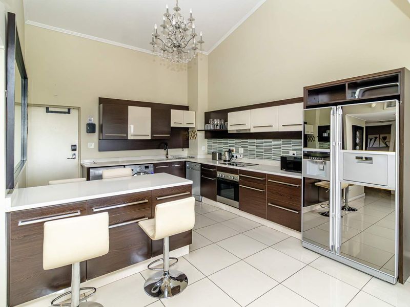 Modern kitchen featuring dark wood cabinetry, stone countertops, integrated appliances, and a breakfast bar, set under a high vaulted ceiling.