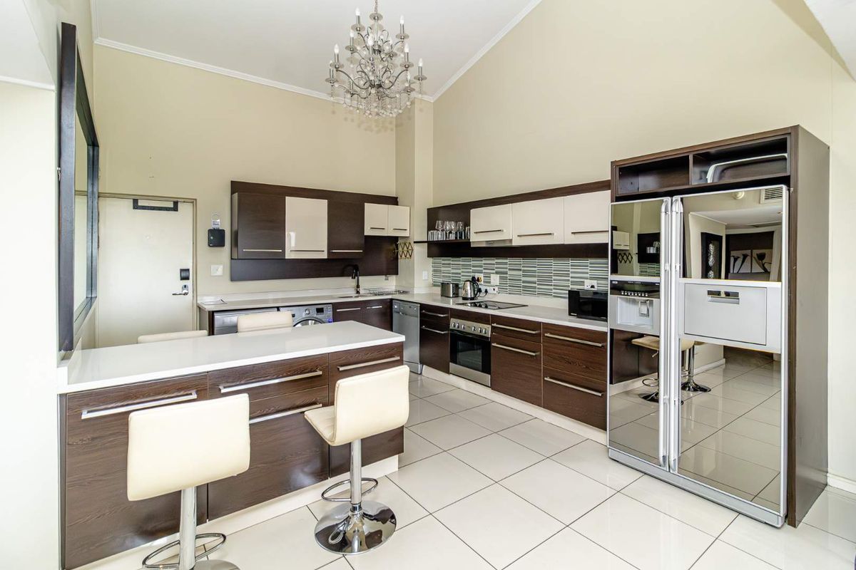 Modern kitchen featuring dark wood cabinetry, stone countertops, integrated appliances, and a breakfast bar, set under a high vaulted ceiling.