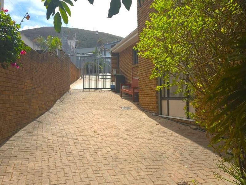 A paved rear exterior walkway featuring brick boundary walls and a secure metal gate entrance.
