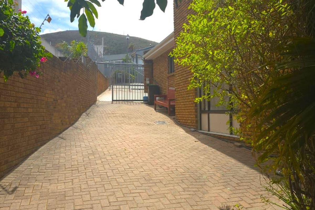 A paved rear exterior walkway featuring brick boundary walls and a secure metal gate entrance.