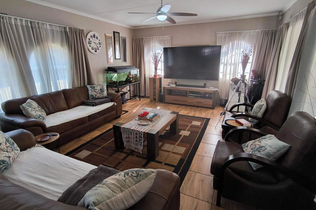 A comfortable living room featuring tiled flooring, a ceiling fan, and large windows with curtains, providing a functional and inviting space for relaxation.