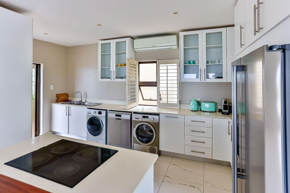 Modern kitchen featuring white cabinetry, stone countertops, integrated appliances, a central island with a ceramic hob, and tiled flooring.