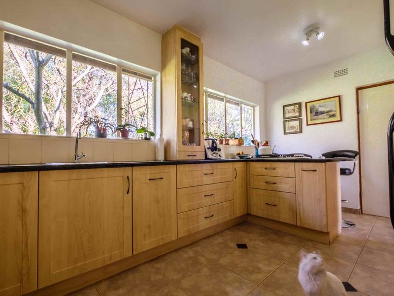 A functional kitchen featuring light wood cabinetry, dark countertops, tiled flooring, and large windows providing ample natural light.