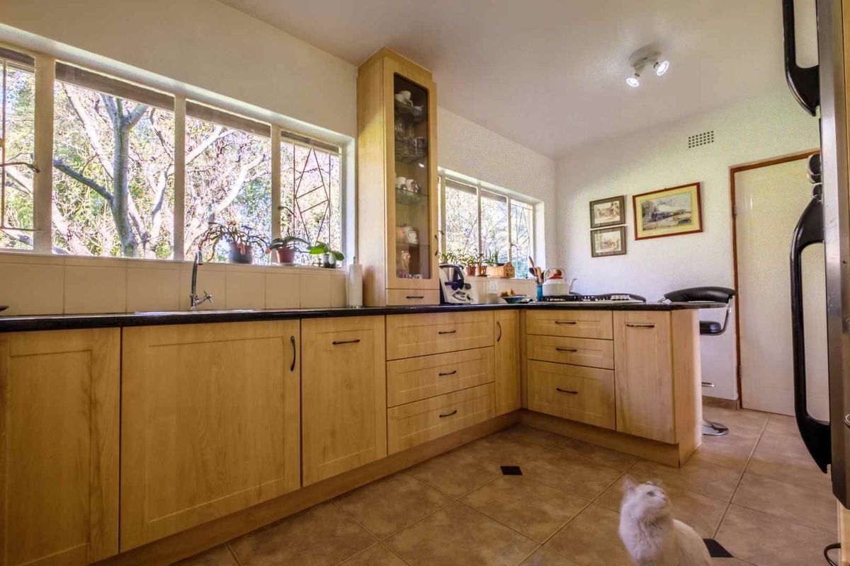 A functional kitchen featuring light wood cabinetry, dark countertops, tiled flooring, and large windows providing ample natural light.