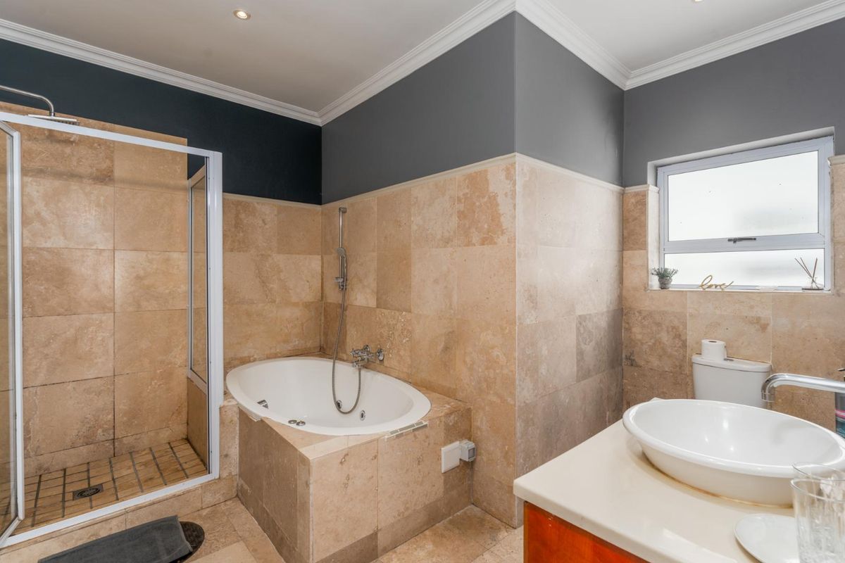 A functional bathroom featuring a built-in bathtub, separate glass-enclosed shower, and a vanity basin with stone-tiled walls and neutral finishes.