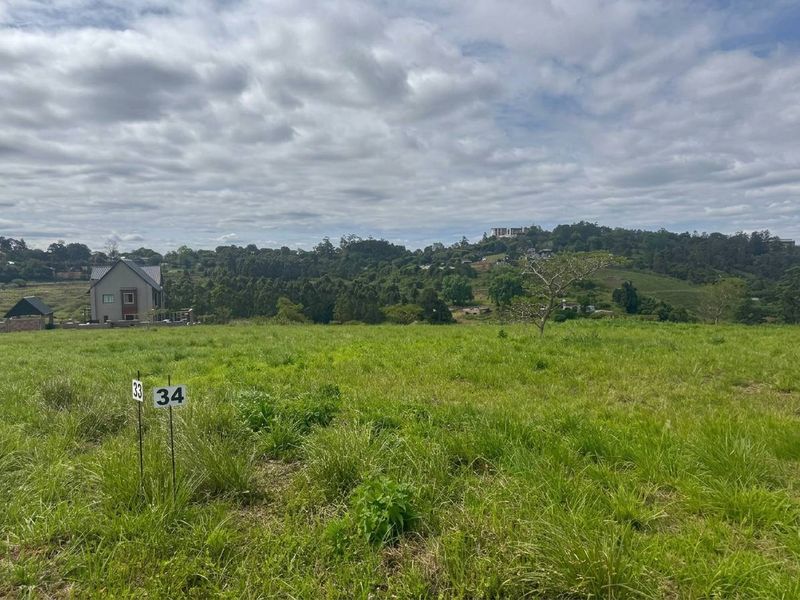 A view of a vacant residential plot featuring natural grassland and boundary markers, set against a scenic hilly landscape.