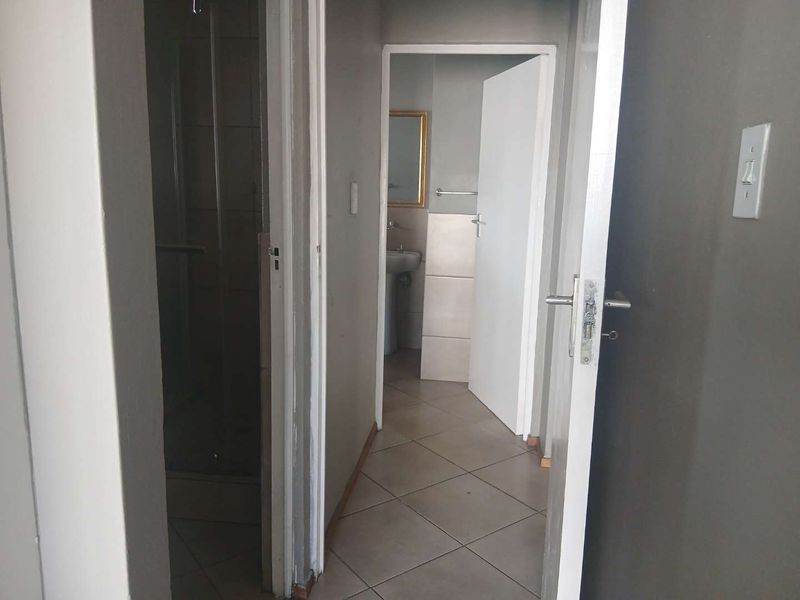 A narrow hallway providing access to a bathroom area with tiled flooring and visible wear on the wall finishes.