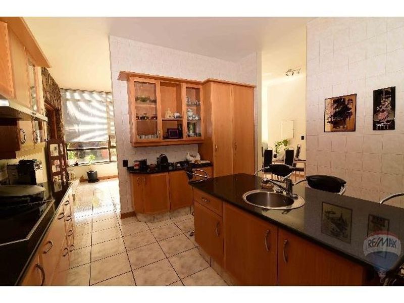 A functional kitchen featuring light wood cabinetry, dark granite countertops, a central island with a prep sink, and tiled flooring.