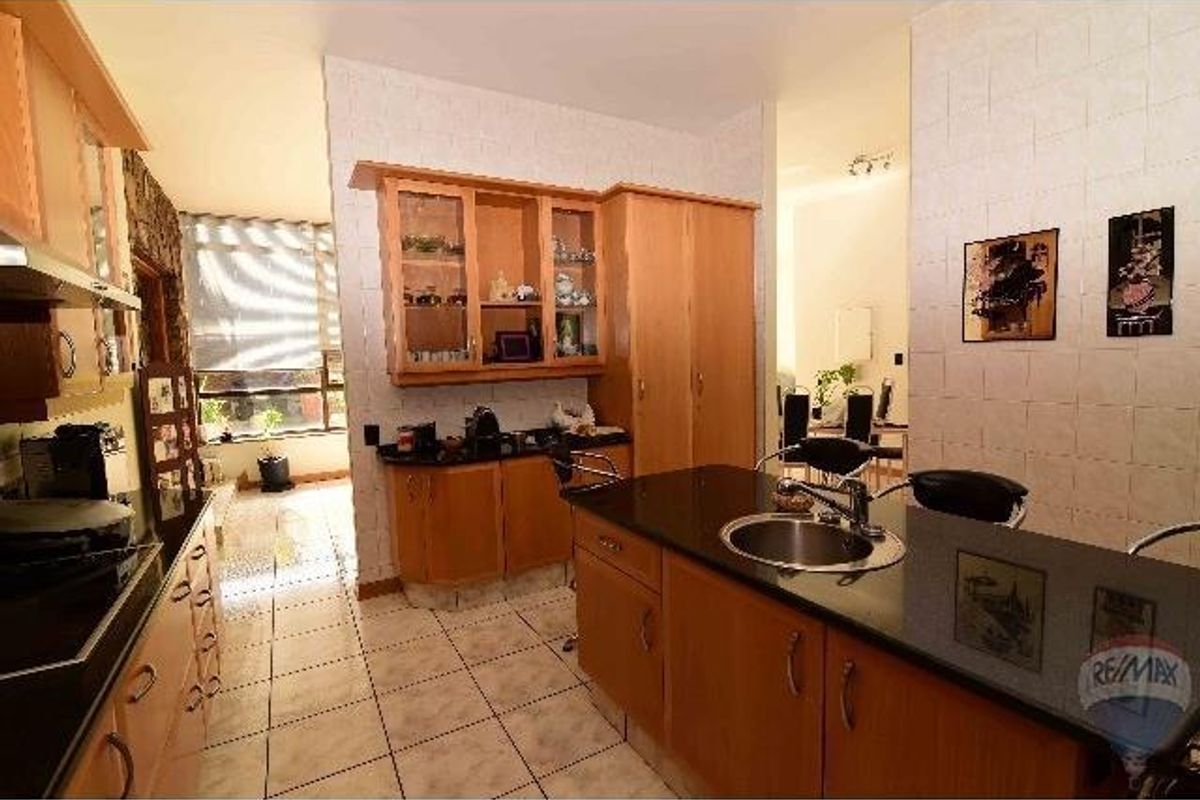 A functional kitchen featuring light wood cabinetry, dark granite countertops, a central island with a prep sink, and tiled flooring.