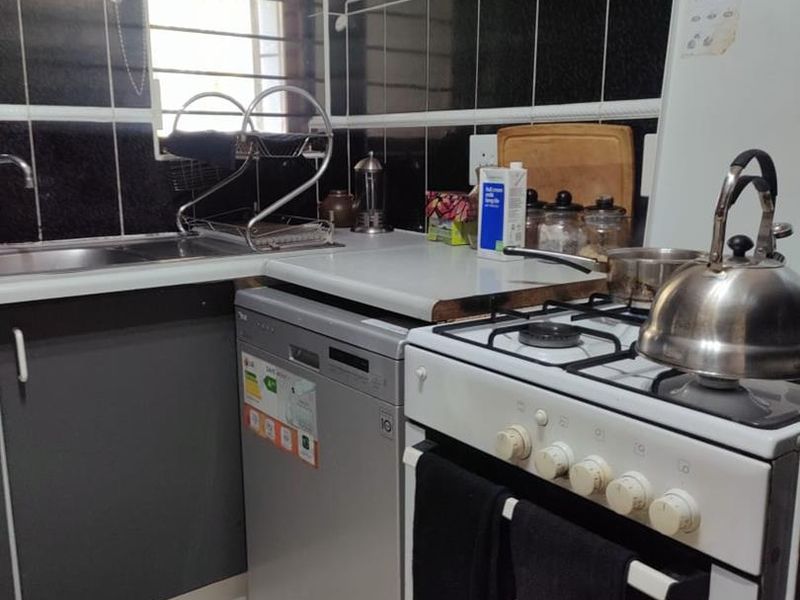 A compact kitchen featuring a gas stove, stainless steel sink, and dark tiled backsplash with built-in cabinetry.