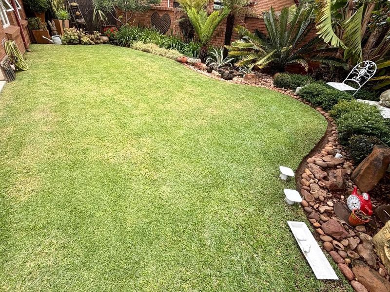 A well-maintained rear garden featuring a lush green lawn, established landscaping, and decorative stone edging along the brick boundary wall.