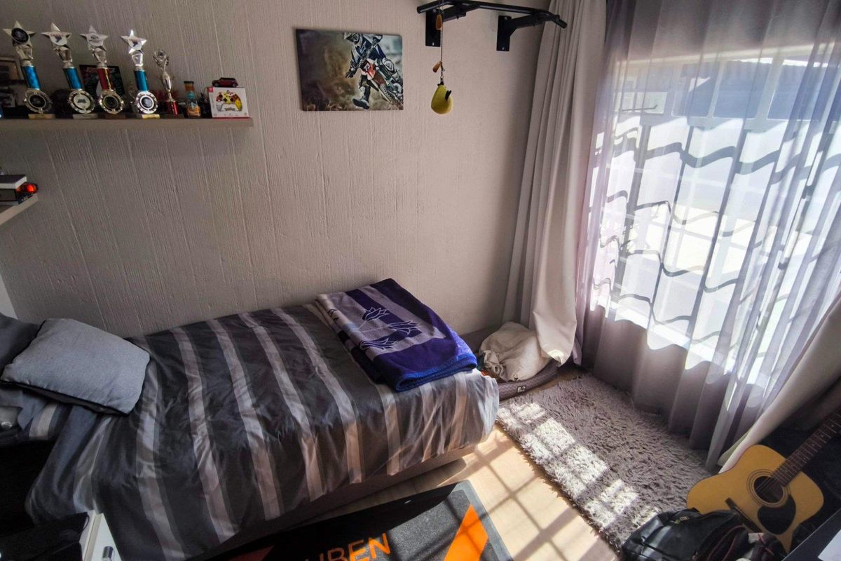 A bedroom featuring a wall-mounted pull-up bar and built-in shelving, with natural light entering through a large window.