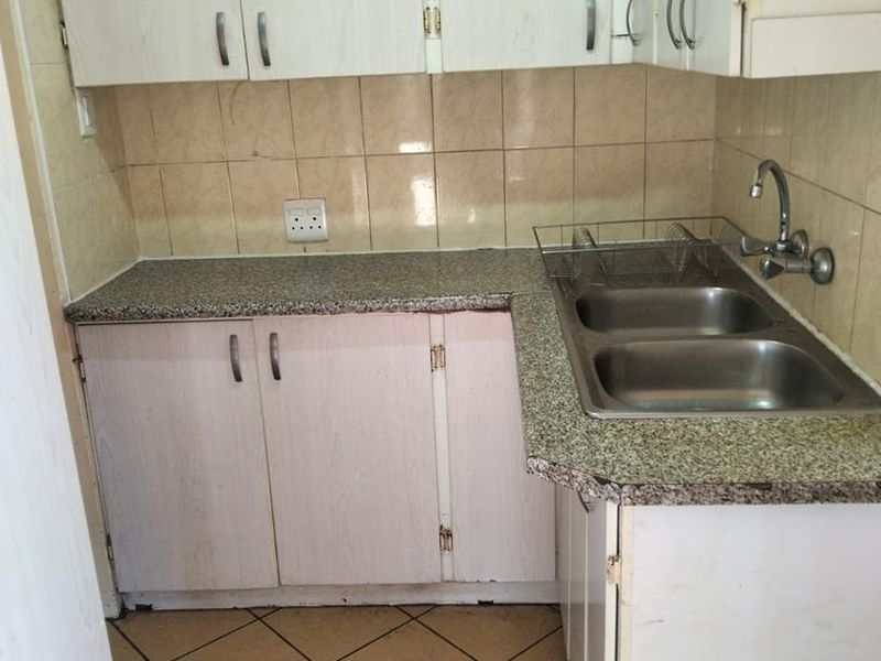 A compact kitchen featuring laminate cabinetry, granite-look countertops, a double stainless steel sink, and ceramic tile flooring.