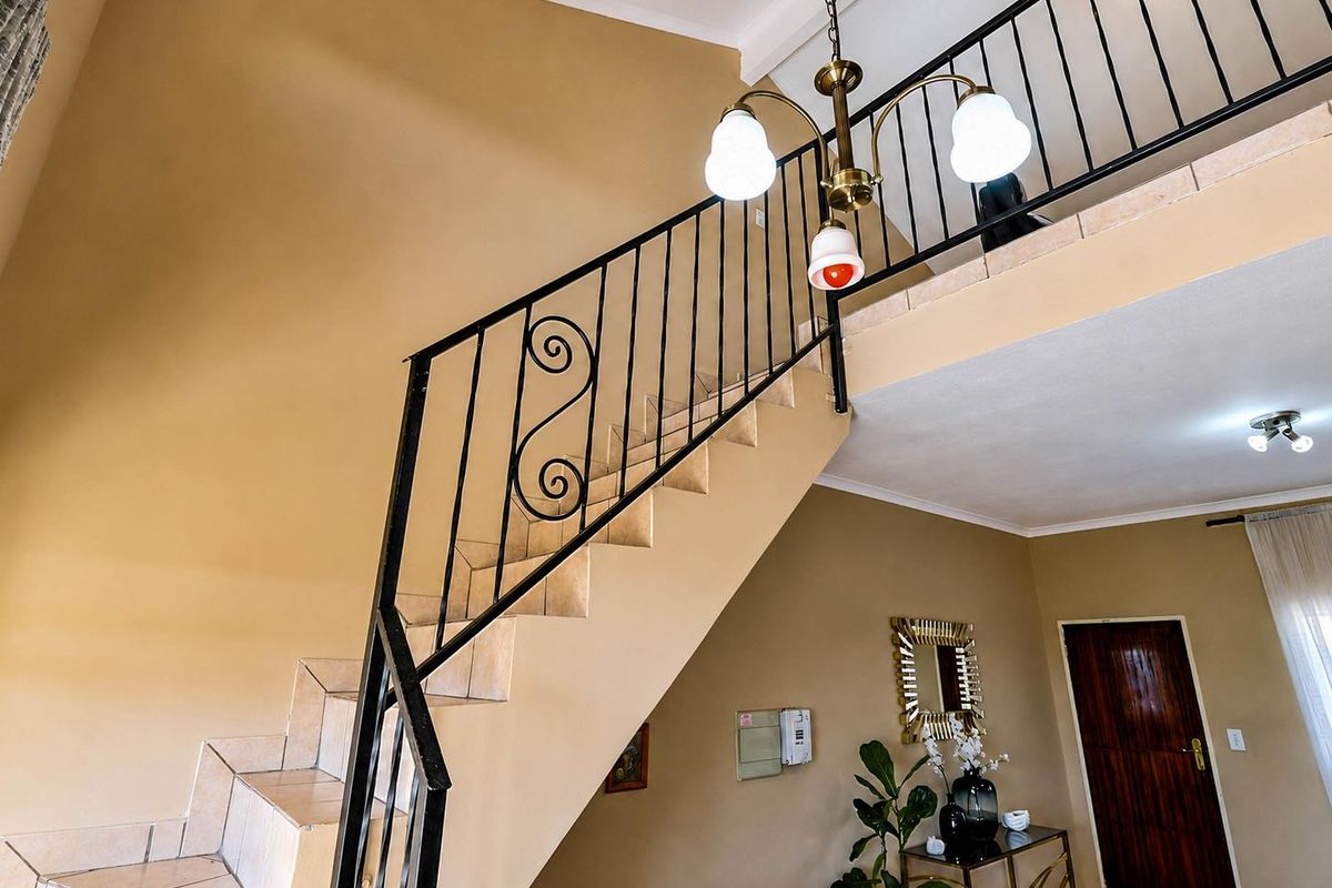 A living area featuring a tiled staircase with a decorative wrought iron balustrade leading to a mezzanine level, complemented by a classic pendant light.