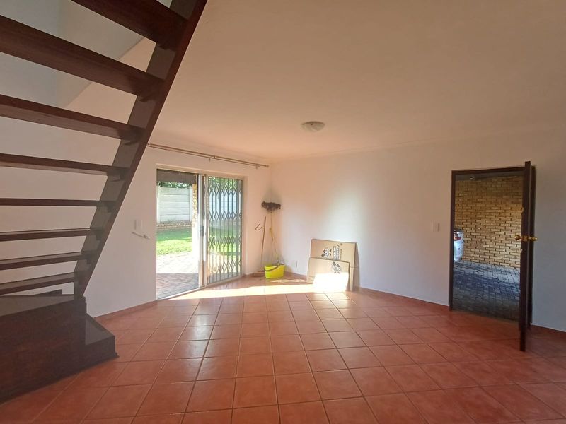 An open-plan living area featuring tiled flooring, a wooden staircase, and a sliding glass door providing access to the outdoor space.