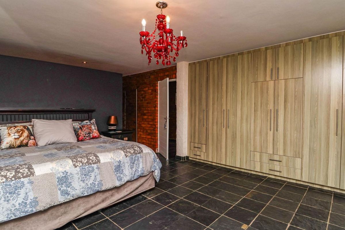 Spacious bedroom featuring built-in wooden cabinetry, dark slate tile flooring, and an exposed brick feature wall.