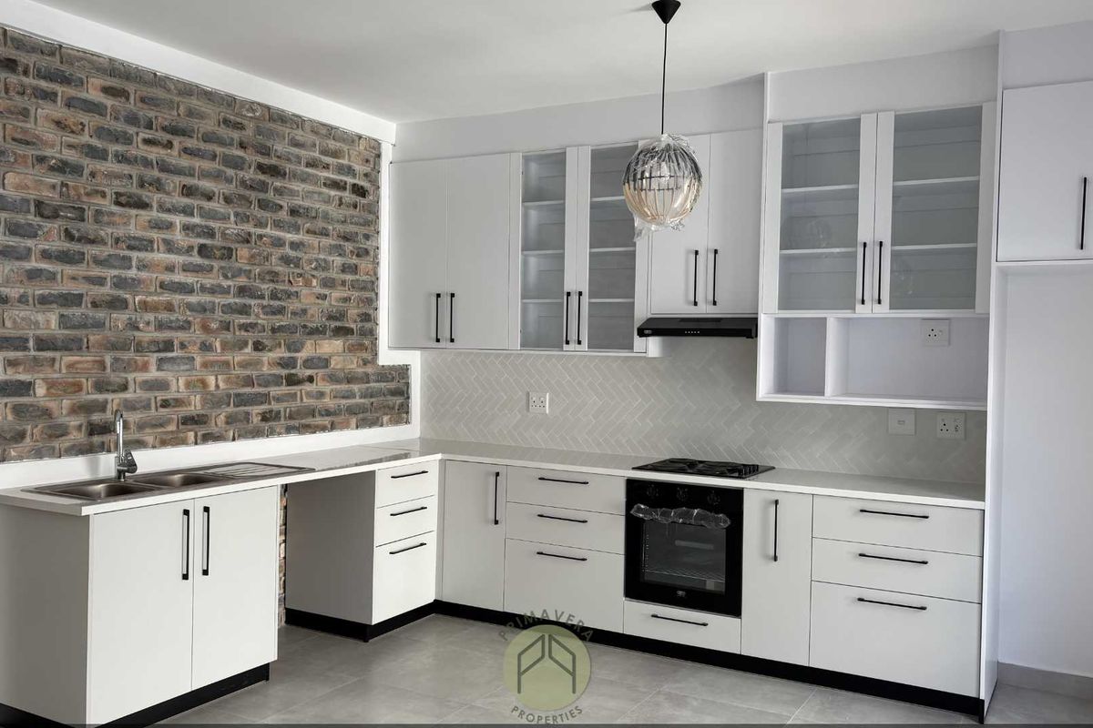 Modern kitchen featuring white cabinetry, stone countertops, a herringbone tile backsplash, and a distinctive exposed brick feature wall.