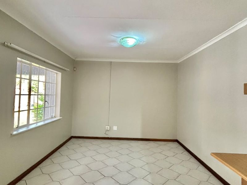 An empty living room featuring neutral walls, tiled flooring, and a window with security bars, offering a blank canvas for interior design.