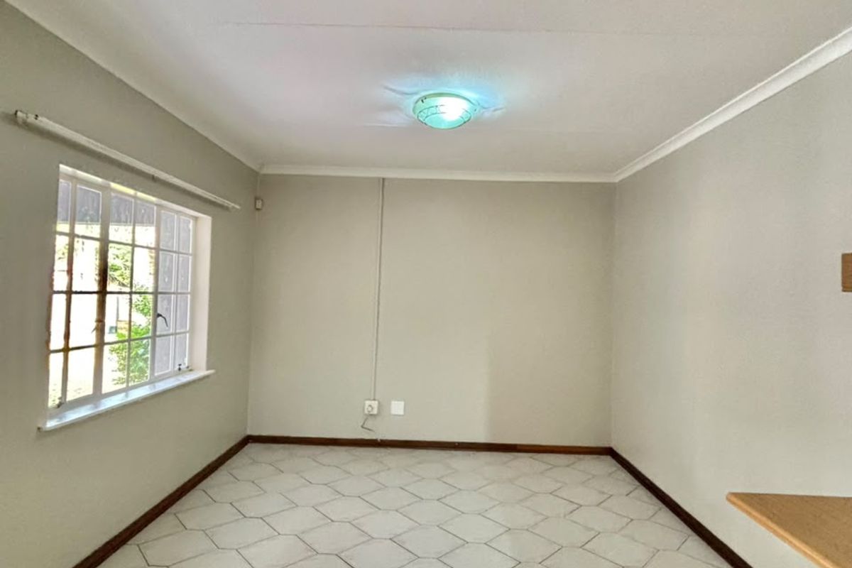 An empty living room featuring neutral walls, tiled flooring, and a window with security bars, offering a blank canvas for interior design.
