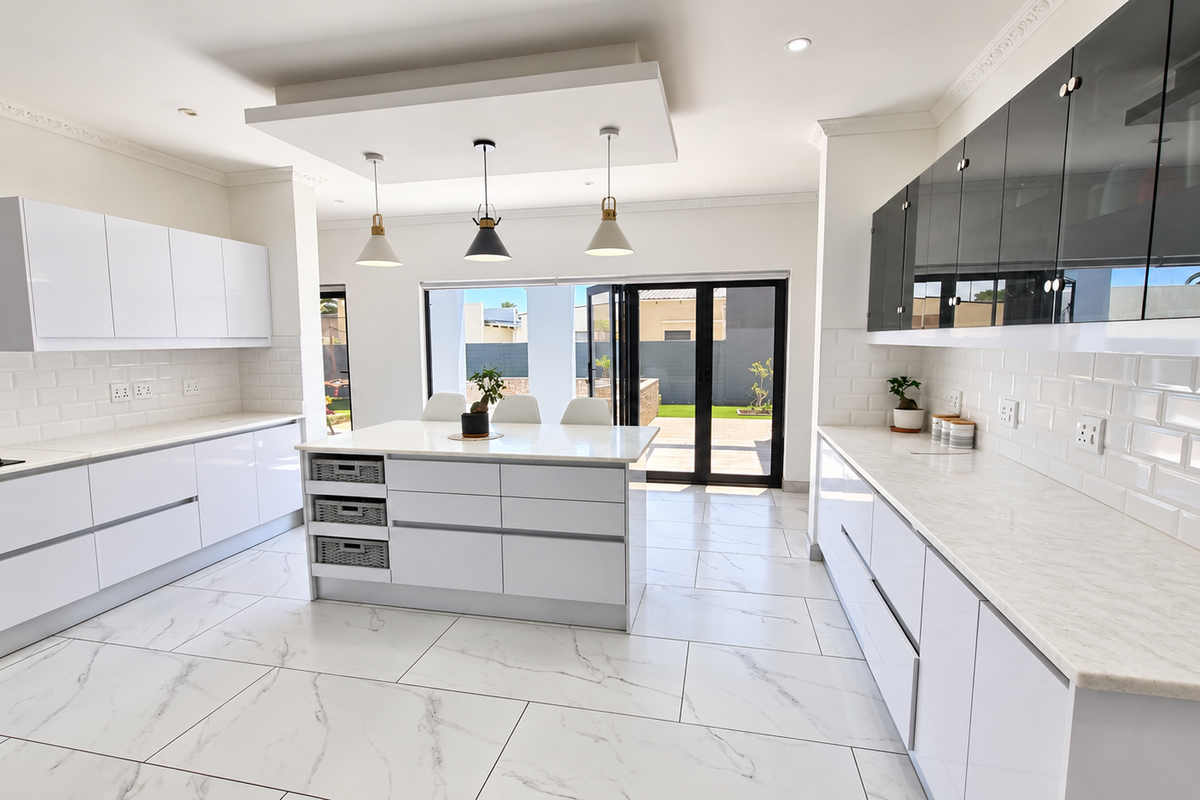 Modern, bright kitchen featuring a central island, white cabinetry, subway tile backsplash, marble-look flooring, and large bi-fold doors opening to the outdoor area.