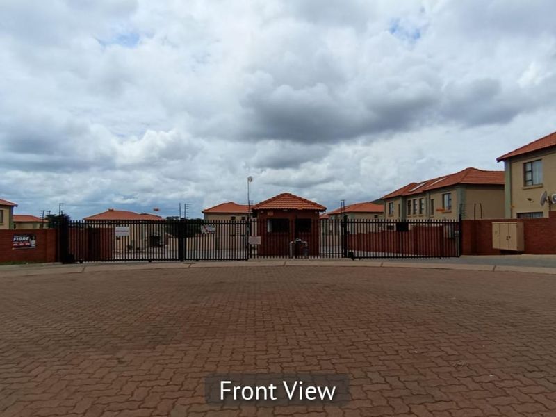 Front view of the residential estate entrance featuring a secure gated access point, guard house, and brick perimeter walling.