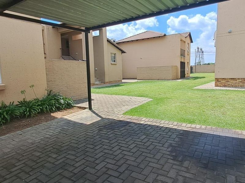 A view of the apartment complex exterior featuring a paved carport area, communal lawn, and external building finishes.