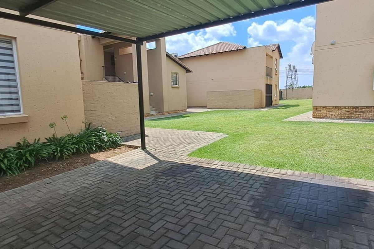 A view of the apartment complex exterior featuring a paved carport area, communal lawn, and external building finishes.