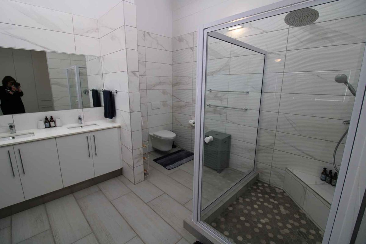 Modern bathroom featuring a double vanity with integrated sinks, a large frameless glass shower enclosure with rainfall showerhead, and contemporary floor-to-ceiling wall tiling.